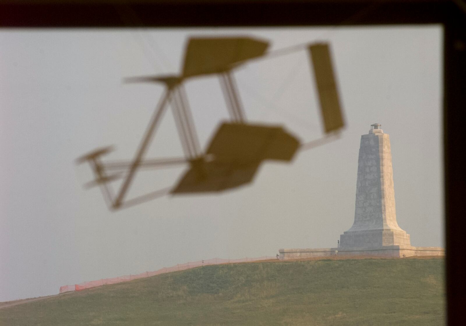 A Wright Flyer model appears to be flying over the Wright Brothers National Memorial from inside the Visitor's Center at Kill Devil Hills. 1997
