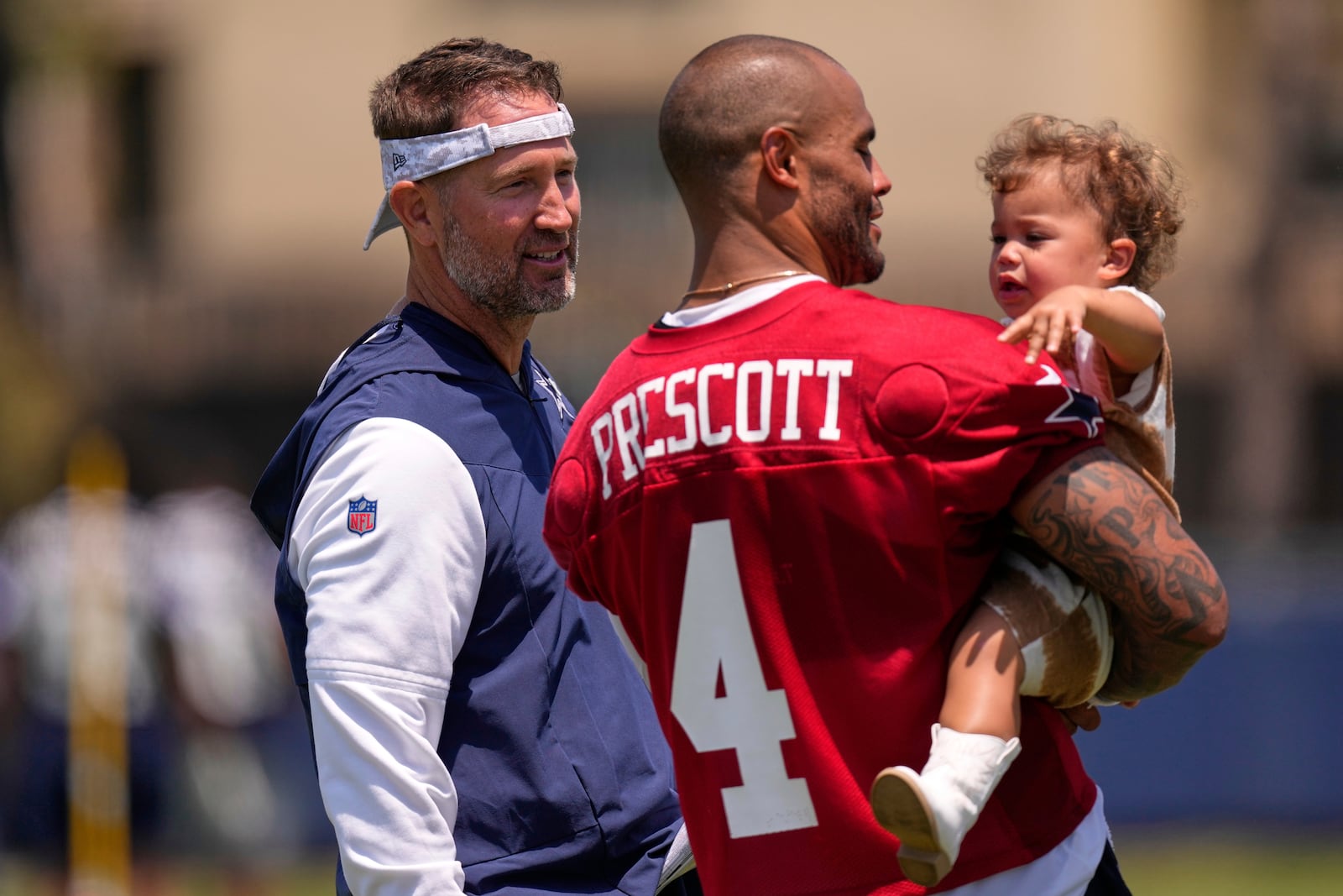 Dallas Cowboys head coach Brian Schottenheimer, left, talks with quarterback Dak Prescott as Prescott holds his daughter Margaret Jane after training camp Tuesday, July 22, 2025, in Oxnard, Calif. (AP Photo/Mark J. Terrill)