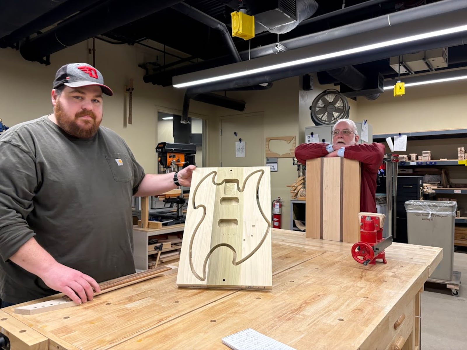 Matt Mongin, instructor at Sinclair Community College, left, with Andrew Shaffer, manager of Sinclair's Guitar Lab, showing a blank outline that guides the shaping of the body of an electric guitar. Students in the Guitar Lab use this and other tools to make their own guitars. THOMAS GNAU/STAFF