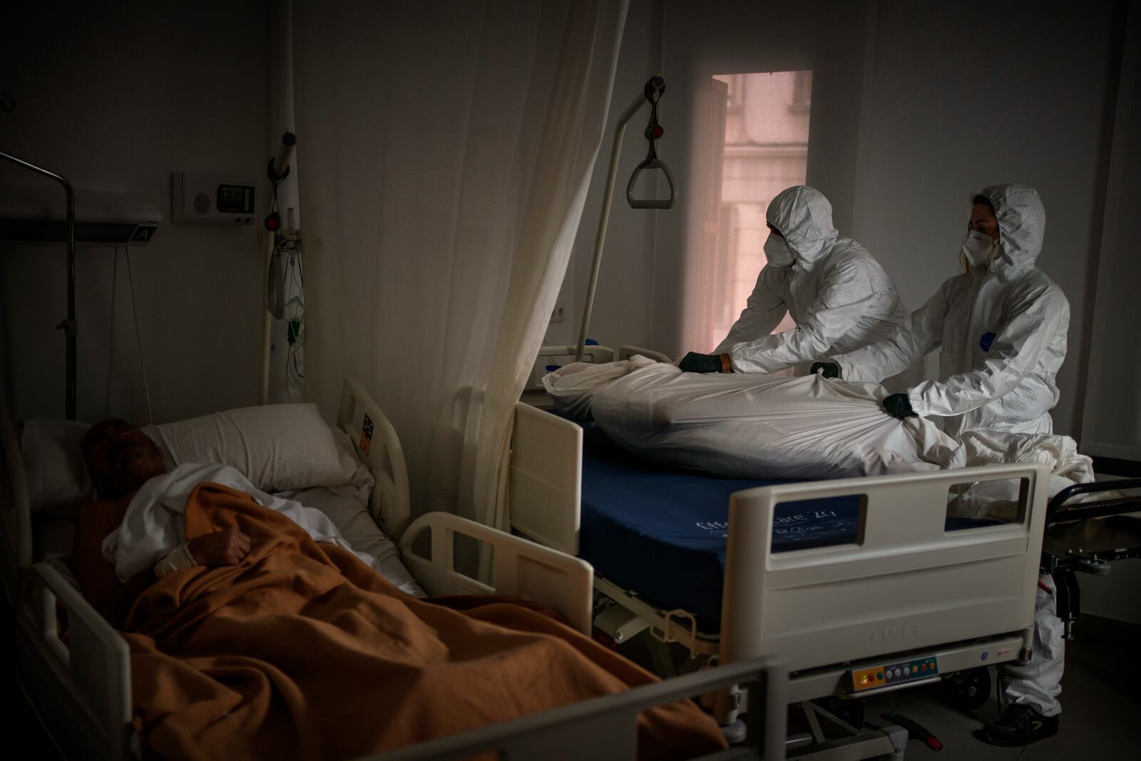 FILE - Wearing protective suits, funeral home workers remove the body of an elderly person who died of COVID-19 at a nursing home while another resident sleeps in his bed in Barcelona, Spain, Thursday, Nov. 5, 2020. (AP Photo/Emilio Morenatti, File)
