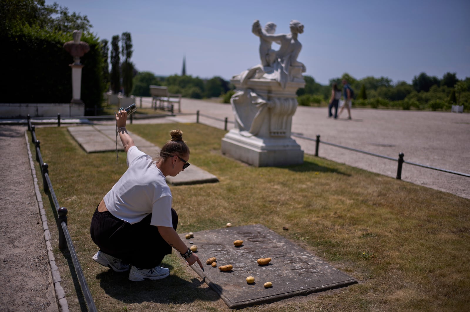 A woman takes a photo of herself as she places a potato on the grave stone of King Frederick II of Prussia, in the park of Sanssouci Palace in Potsdam, Germany, June 17, 2025. (AP Photo/Markus Schreiber)