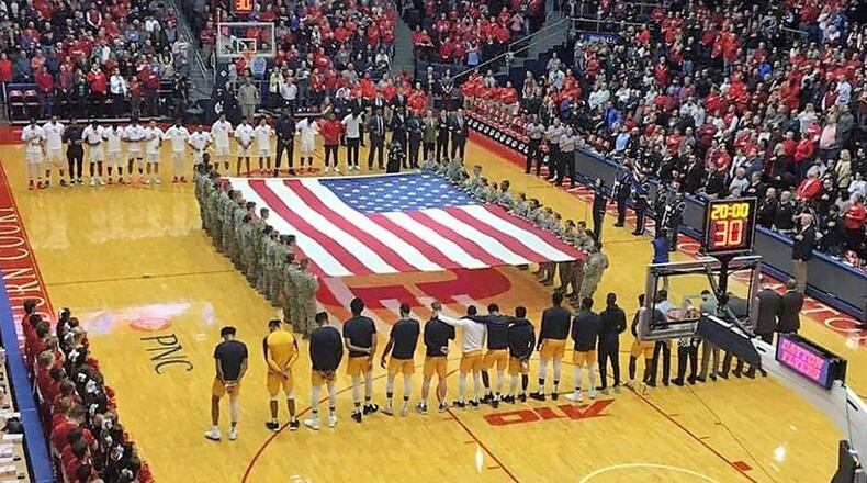 Wright-Patterson Band of Flight vocalist Staff Sgt. Joanne Griffin sings the national anthem while the base Honor Guard presents the colors, and students from the United States Air Force School of Aerospace Medicine and University of Dayton ROTC hold a large U.S. flag in the center of the court during the pregame ceremonies at the University of Dayton men’s basketball game Nov. 10. (Contributed photo)