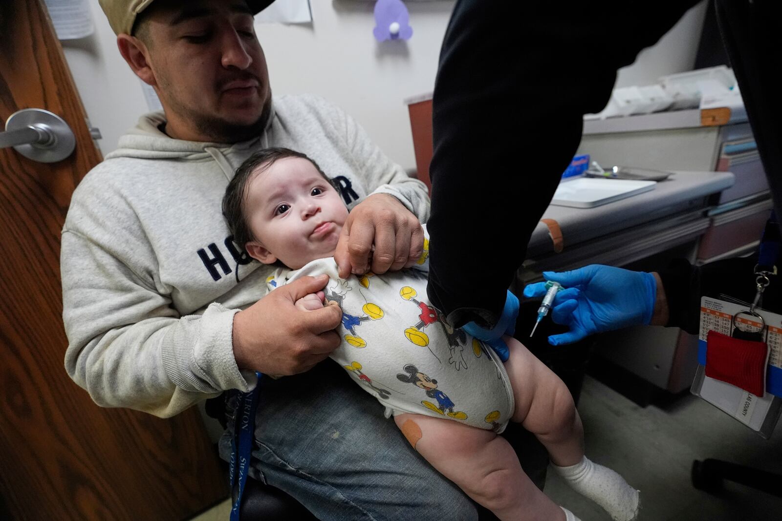 Cesar Acevedo, left, holds his infant son, Adriel Acevedo, as as nurse Tracey McElroy, right, prepares to give him a vaccination that included a polio dose at the Dallas County Health and Human Services immunization clinic in Dallas, Friday, April 4, 2025. (AP Photo/LM Otero)