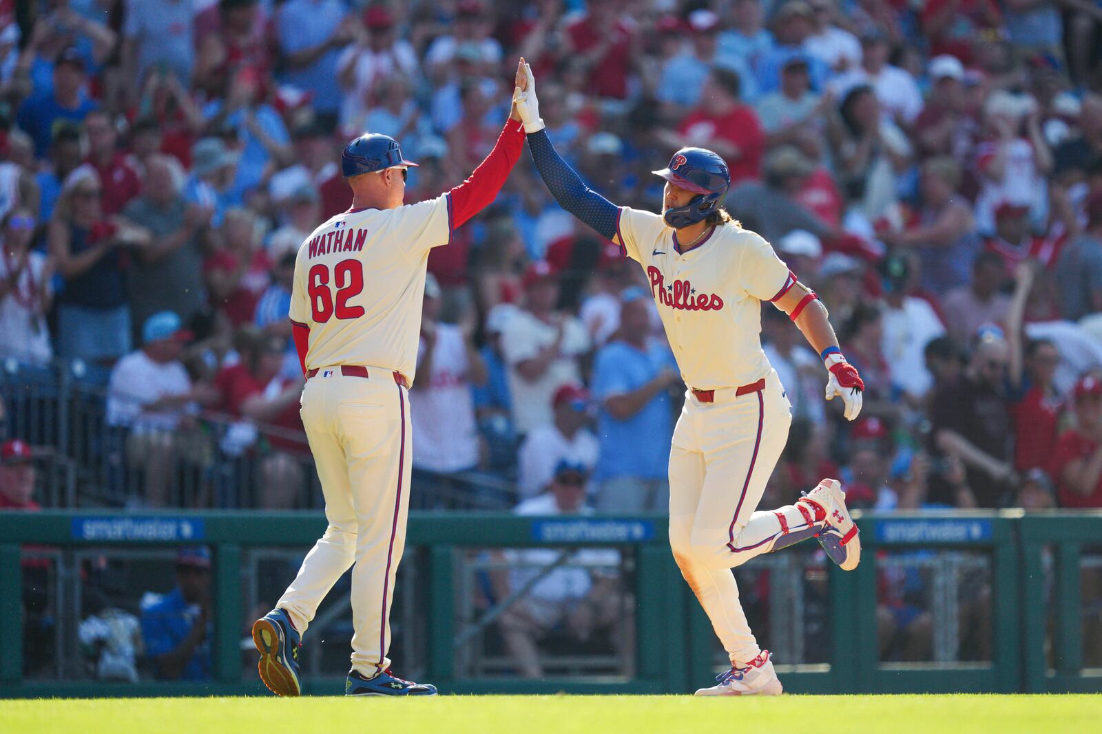 Philadelphia Phillies' Alec Bohm, right, high-fives third base coach Dusty Wathan (62) after hitting a two-run home run during the sixth inning of a baseball game against the Cincinnati Reds, Saturday, July 5, 2025, in Philadelphia. (AP Photo/Derik Hamilton)