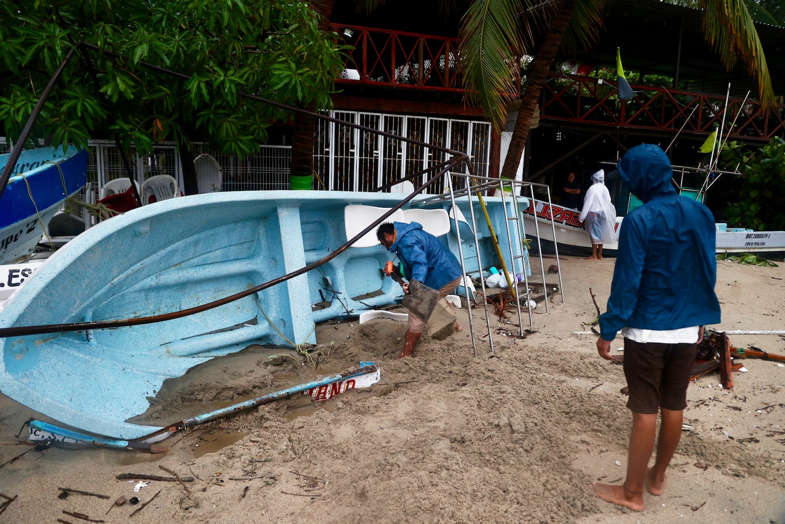 A person removes sand from a boat that was taken offshore in preparation for Hurricane Erick after the storm hit near Puerto Escondido, Oaxaca state, Mexico, Thursday, June 19, 2025. (AP Photo/Luis Alberto Cruz)