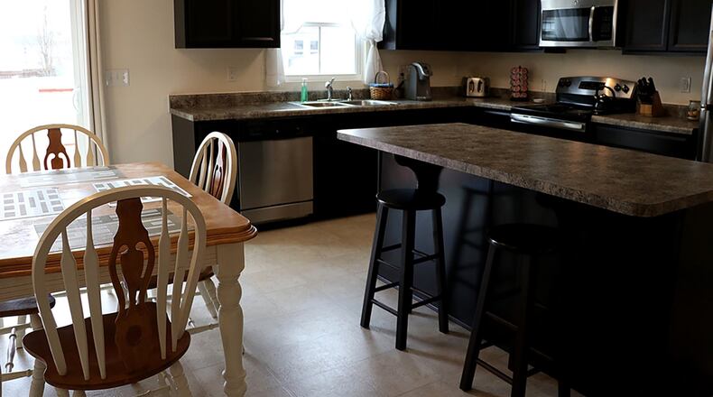 Espresso-stained cabinets frame the kitchen’s work space, which takes an “L-shape” as it wraps around a corner with complementary work counters.