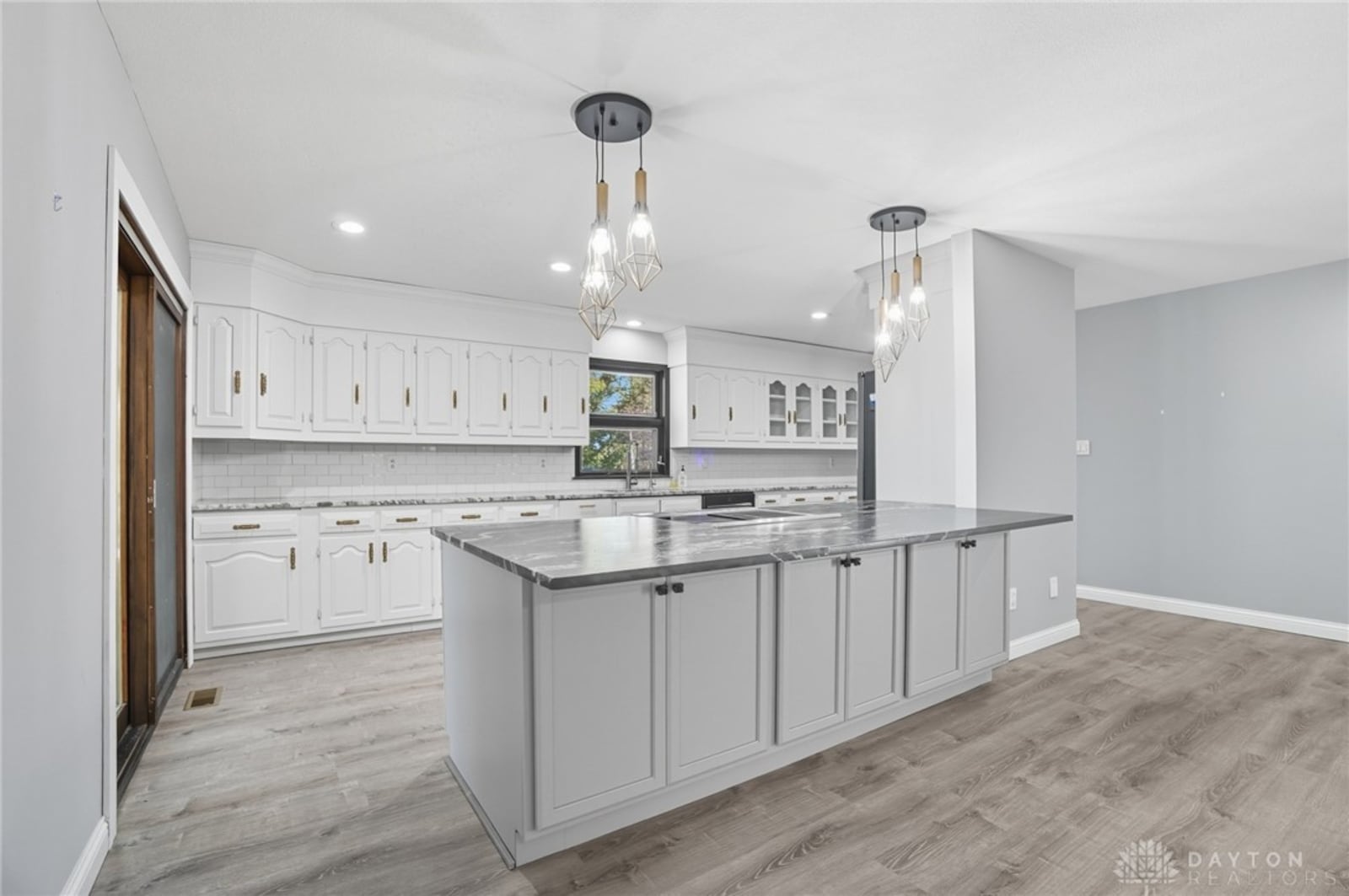 The kitchen has been completely updated and includes white cabinetry, an island with seating and new lighting fixtures, recessed lighting and LVT flooring. a sliding glass door opens to the screened in porch. CONTRIBUTED