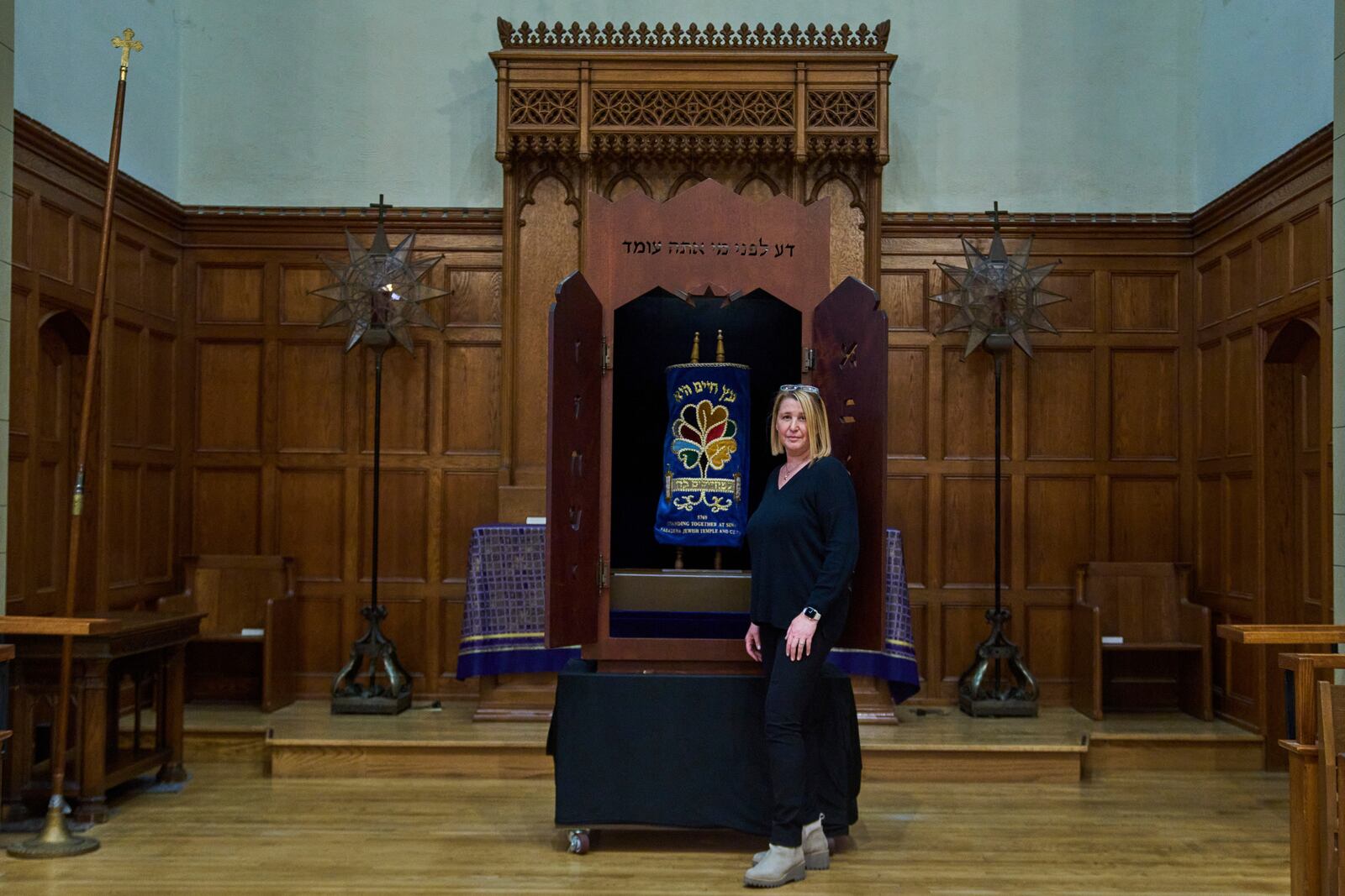 Cantor Ruth Berman Harris poses for a photo by her temple's Torah scrolls from their Pasadena Jewish Temple and Center that burned in the Eaton fire, at a temporary chapel at the First United Methodist Church where she is preparing her congregation for Passover Seder in Pasadena, Calif., Friday, April 4, 2025. (AP Photo/Damian Dovarganes)