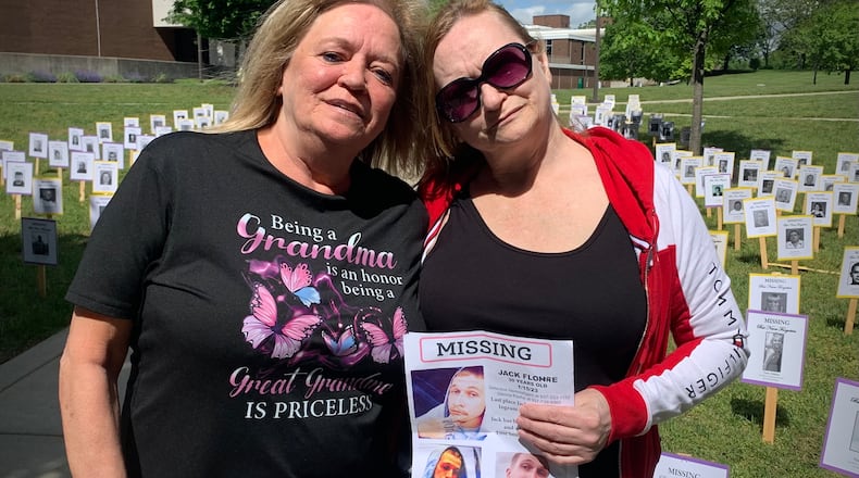 From left: stepmother Karen Flohre, and mother Glenna Flohre hold a poster of Jack Flohre, a Dayton man who has been missing for more than two years. Behind them are pictures of Ohio's missing persons, assembled on the lawn at Wright State University for a commemorative event, Saturday, May 17, 2025. LONDON BISHOP/STAFF