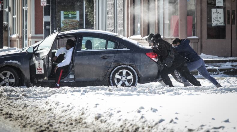 Good Samaritans help push a driver out of the ally on Brown St. Tuesday morning after a powerful winter storm dumped copious amounts of snow in the Miami Valley.