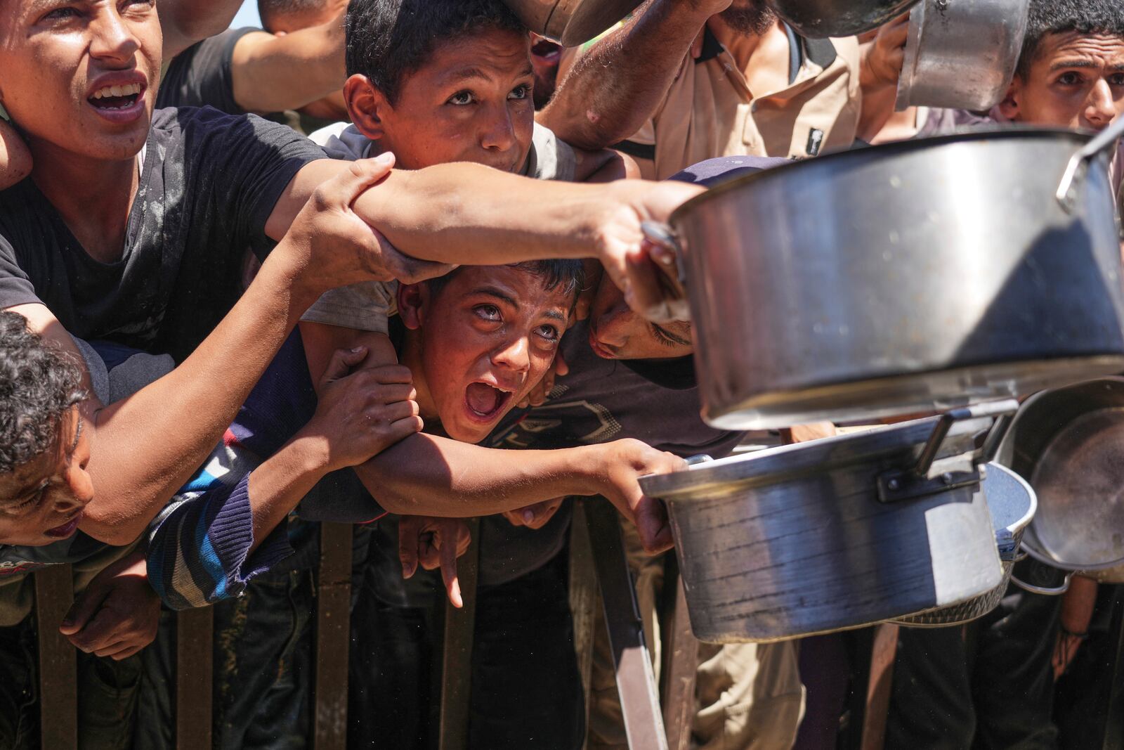Palestinians struggle to receive cooked food distributed at a community kitchen in the Muwasi area of Khan Younis, in the Gaza Strip, Friday, May 23, 2025. (AP Photo/Abdel Kareem Hana)