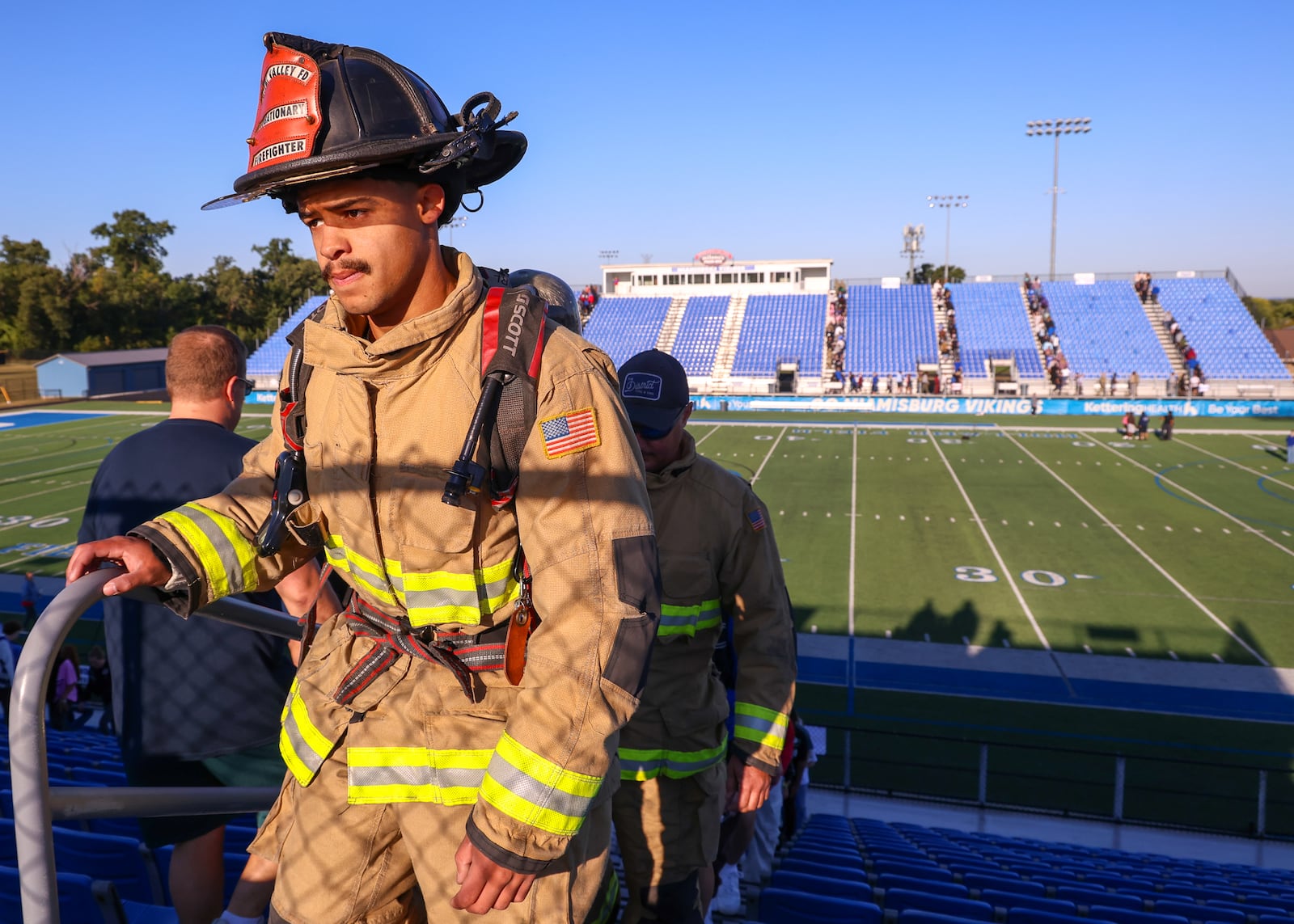 A Miami Valley Fire District firefighter leads a group up stairs at Holland Field during Miamisburg High School's fifth annual 9/11 Memorial Stair Climb on Monday, Sept. 8, 2025. Students, staff, first responders and military service members climbed bleachers in honor of those who died during the Sept. 11 attacks, each carrying a card with a victim’s name. BRYANT BILLING / STAFF