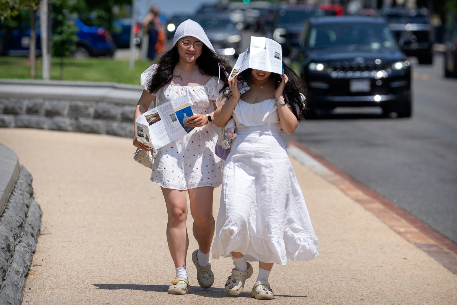 Visitors use brochures to shield themselves from the sun as they walk near the U.S. Capitol on an unseasonably hot day, Tuesday, June 24, 2025, in Washington. (AP Photo/Mark Schiefelbein)