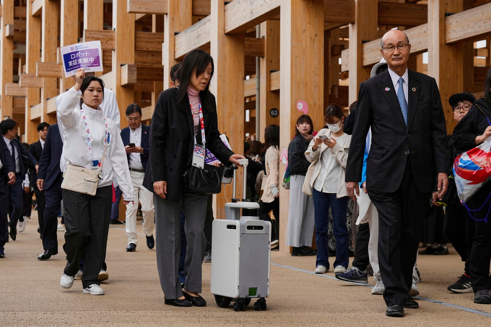 An organizer, center, uses a robot to help navigate those who have visual Impairment, as they show its testing at the Expo 2025 on the opening day in Osaka, central Japan, Sunday, April 13, 2025. (AP Photo/Hiro Komae)