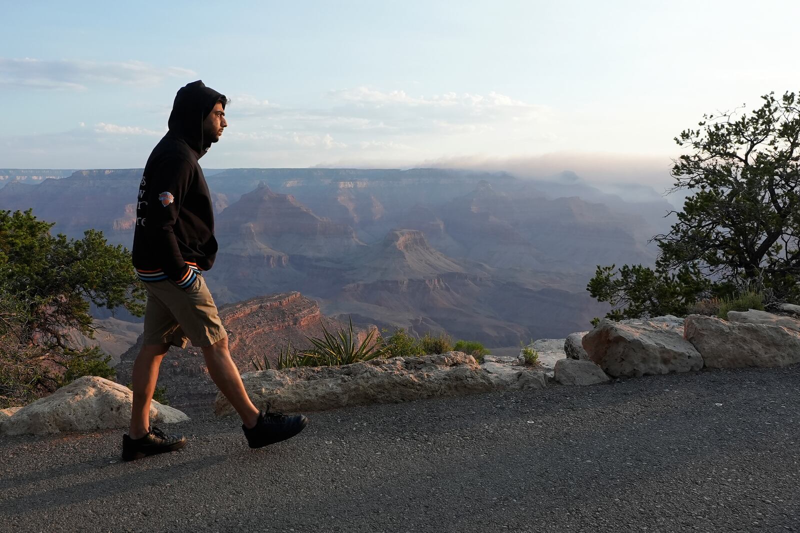 A tourist takes in the morning sunrise from the South Rim as smoke from the Dragon Bravo Fire moves over the Grand Canyon from the North Rim Tuesday, July 15, 2025, in Grand Canyon National Park, Ariz. (AP Photo/Ross D. Franklin)