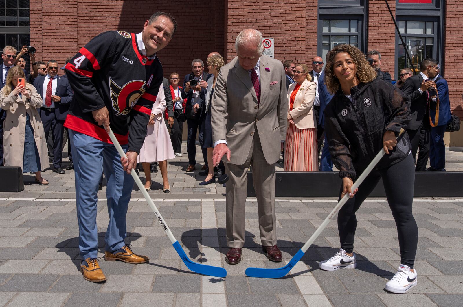 King Charles participate in a ceremonial puck drop with street hockey captains Chris Phillips, left and Desiree Scott during a visit to Lansdowne Park in Ottawa, Canada on Monday, May 26, 2025. (Christinne Muschi/The Canadian Press via AP)