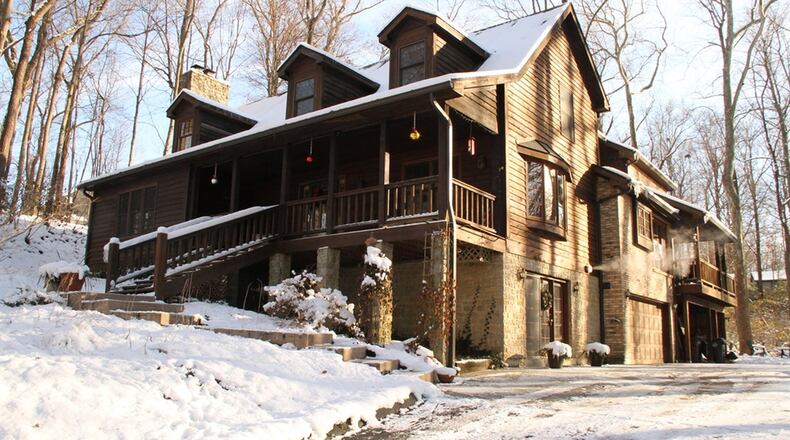 Rooftop dormers and side-entry garage doors blend in with the stone-trimmed cedar wood construction of this Washington Twp. two-story lodge style home set on a nearly two-acre property with a creek running through it. Stone pillars support the raised front porch under a steep rooftop with three dormer windows.