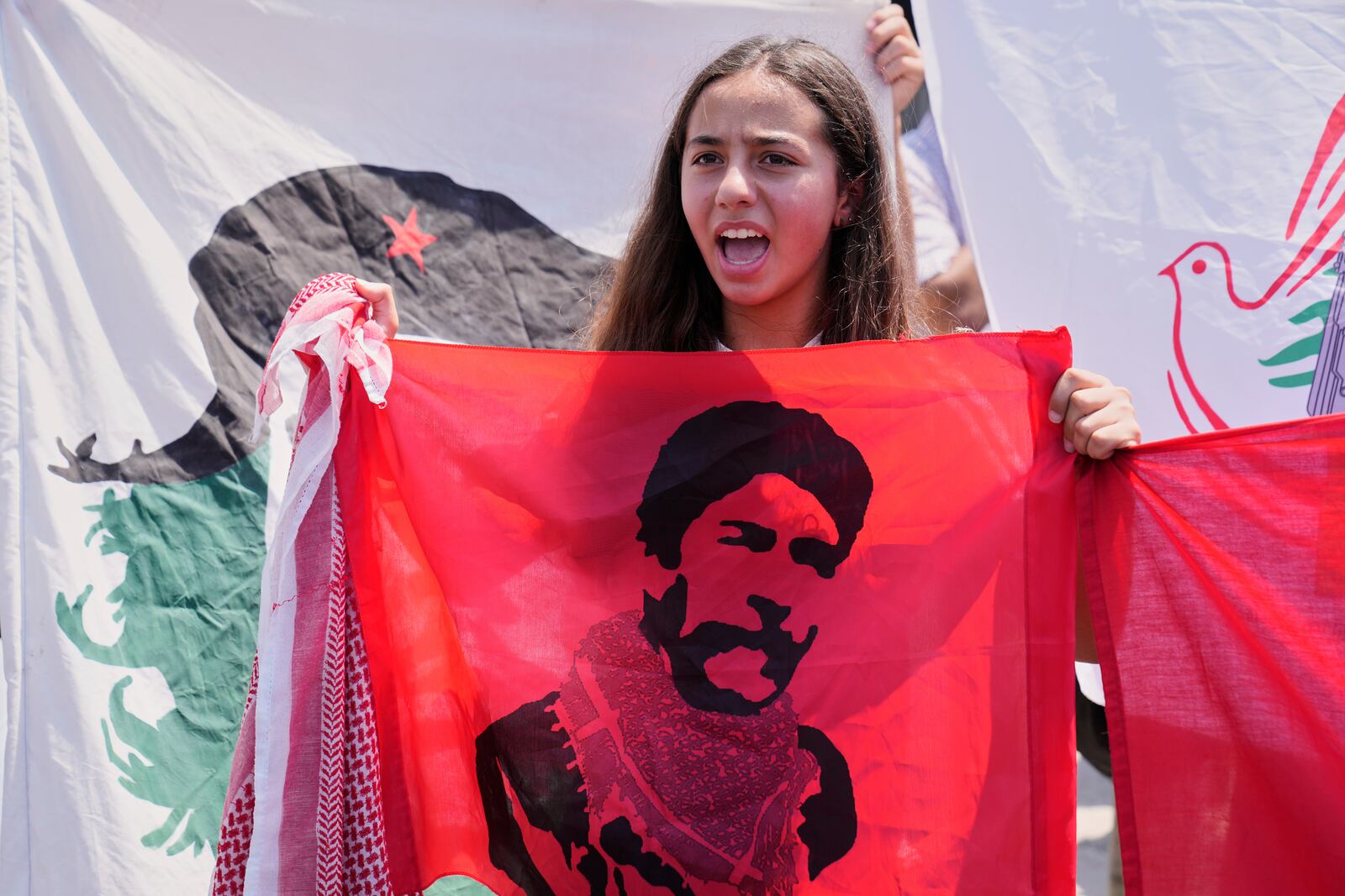 A supporter of Lebanese pro-Palestinian militant George Abdallah, pictured on the flag, who was serving a life sentence for complicity in the 1982 murders of an American and an Israeli diplomat in Paris, shouts slogans as she waits for his arrival at Rafic Hariri International Airport in Beirut, Lebanon, Friday, July 25, 2025. (AP Photo/Hussein Malla)