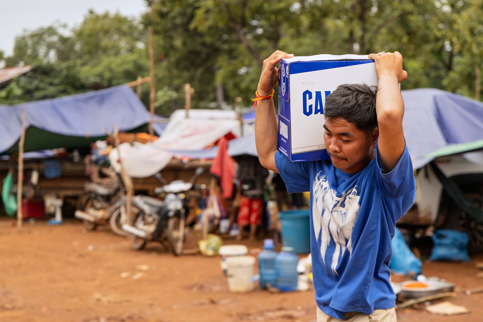 A man carries a box of water handed out at the Battkhao Resettlement Camp for displaced Cambodians in Oddar Meanchey Province on Saturday, July 26, 2025. (AP Photo/Anton L. Delgado)