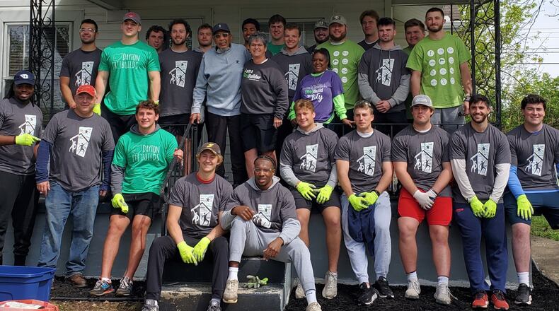 Dayton Flyers football players gather around former Roosevelt High football star Charles Harden, who was named the city’s Mr. Football in 1958, and Cathy Spaugy, project manager of Rebuild Dayton Together effort, on the front porch of Harden’s home. Tom Archdeacon/CONTRIBUTED