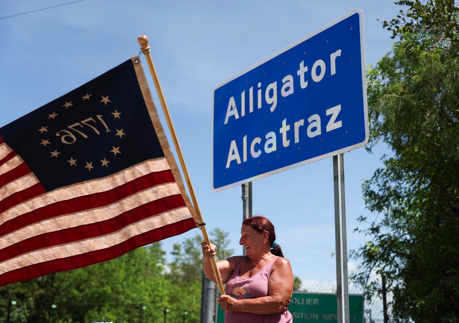 Rana Mourer waves an American flag outside of the migrant detention facility dubbed "Alligator Alcatraz," at the Dade-Collier Training and Transition facility, Saturday, July 12, 2025 in Ochopee, Fla. (AP Photo/Alexandra Rodriguez)