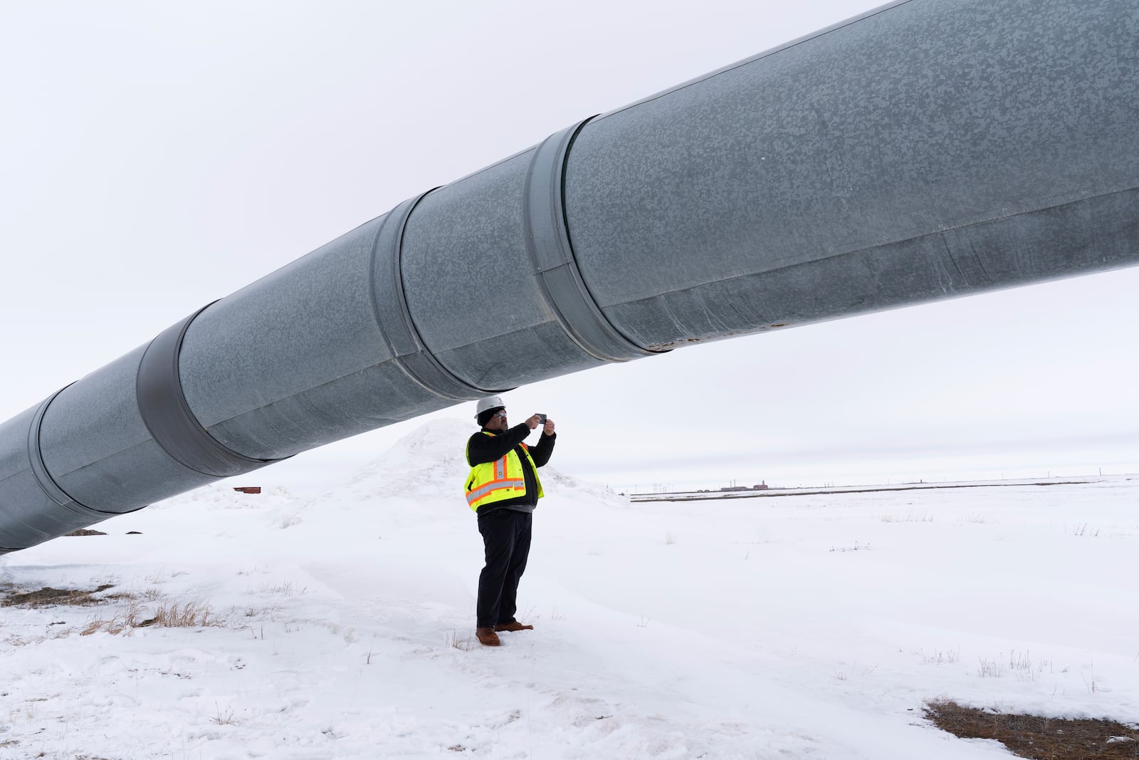 A worker takes a photo under the start of the Trans-Alaska Pipeline after a news conference at the Pump Station 1 on Monday, June 2, 2025, located near Deadhorse, Alaska, on the state's prodigious North Slope. (AP Photo/Jenny Kane)
