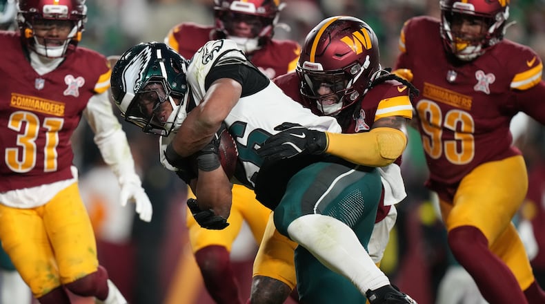 Philadelphia Eagles running back Saquon Barkley, center left, runs for a touchdown against Washington Commanders cornerback Noah Igbinoghene, center right, during the second half of an NFL football game, Saturday, Dec. 20, 2025, in Landover, Md. (AP Photo/Stephanie Scarbrough)