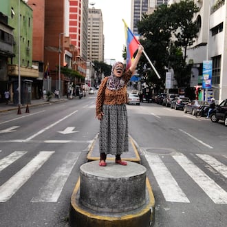 A supporter of Venezuelan President Nicolas Maduro stands on a median strip waving a national flag in Caracas, Venezuela, Saturday, Jan. 3, 2026, after U.S. President Donald Trump announced that Maduro had been captured and flown out of the country. (AP Photo/Ariana Cubillos)
