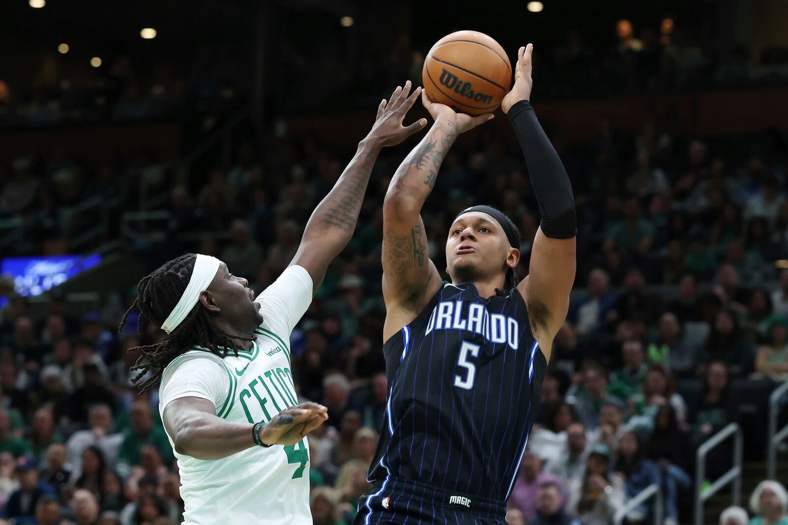 Orlando Magic's Paolo Banchero (5) shoots against Boston Celtics' Jrue Holiday (4) during the second half in Game 1 of a first-round NBA playoff basketball series Sunday, April 20, 2025, in Boston. (AP Photo/Michael Dwyer)