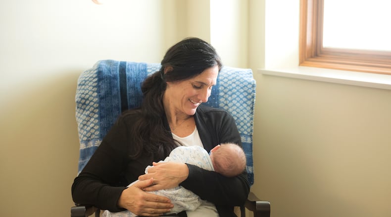A smiling woman seated in a rocking chair cradles a newborn infant.
