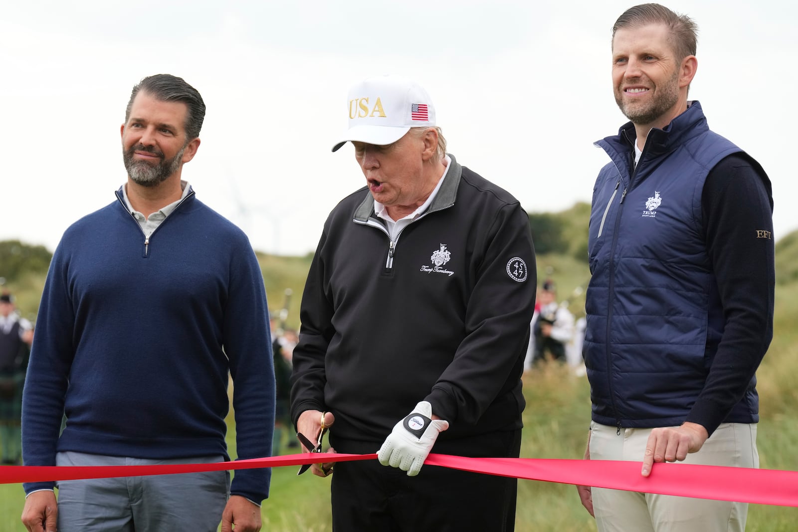 President Donald Trump cuts the ribbon, standing between Donald Trump Jr., left, and Eric Trump, during an opening ceremony for the Trump International Golf Links golf course, near Aberdeen, Scotland, Tuesday, July 29, 2025. (AP Photo/Jacquelyn Martin)