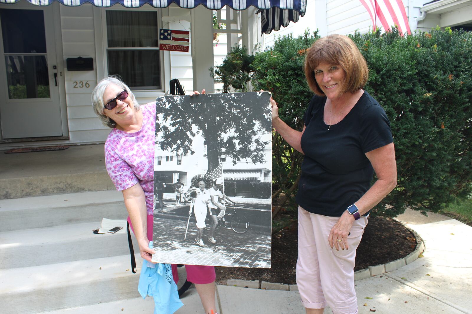 Dayton Wroe Avenue will celebrate the 50th anniversary of its  Labor Day weekend Block party on Sunday, Aug 3, 2017. Wroe Avenue residents Virginia Platt Gehres and Ann Szabo hold a poster of Szabo's mother, Ann Moore, as grand marshal of the block party.  The women grew up on the street and now call it home.