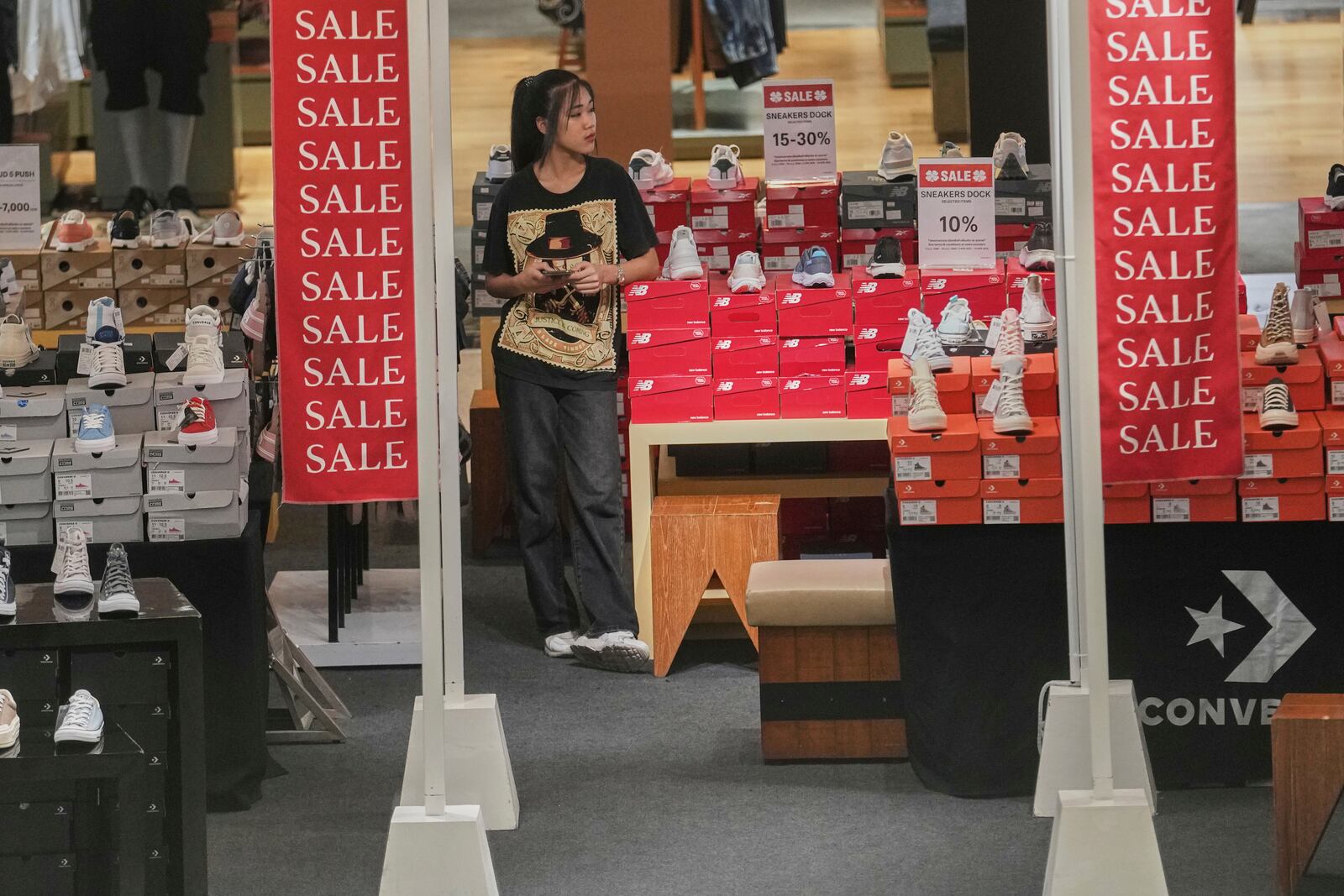 A shop clerk waits for customers behind a sales advertisement at a shopping mall in Bangkok, Thailand, Wednesday, April 9, 2025. (AP Photo/Sakchai Lalit)
