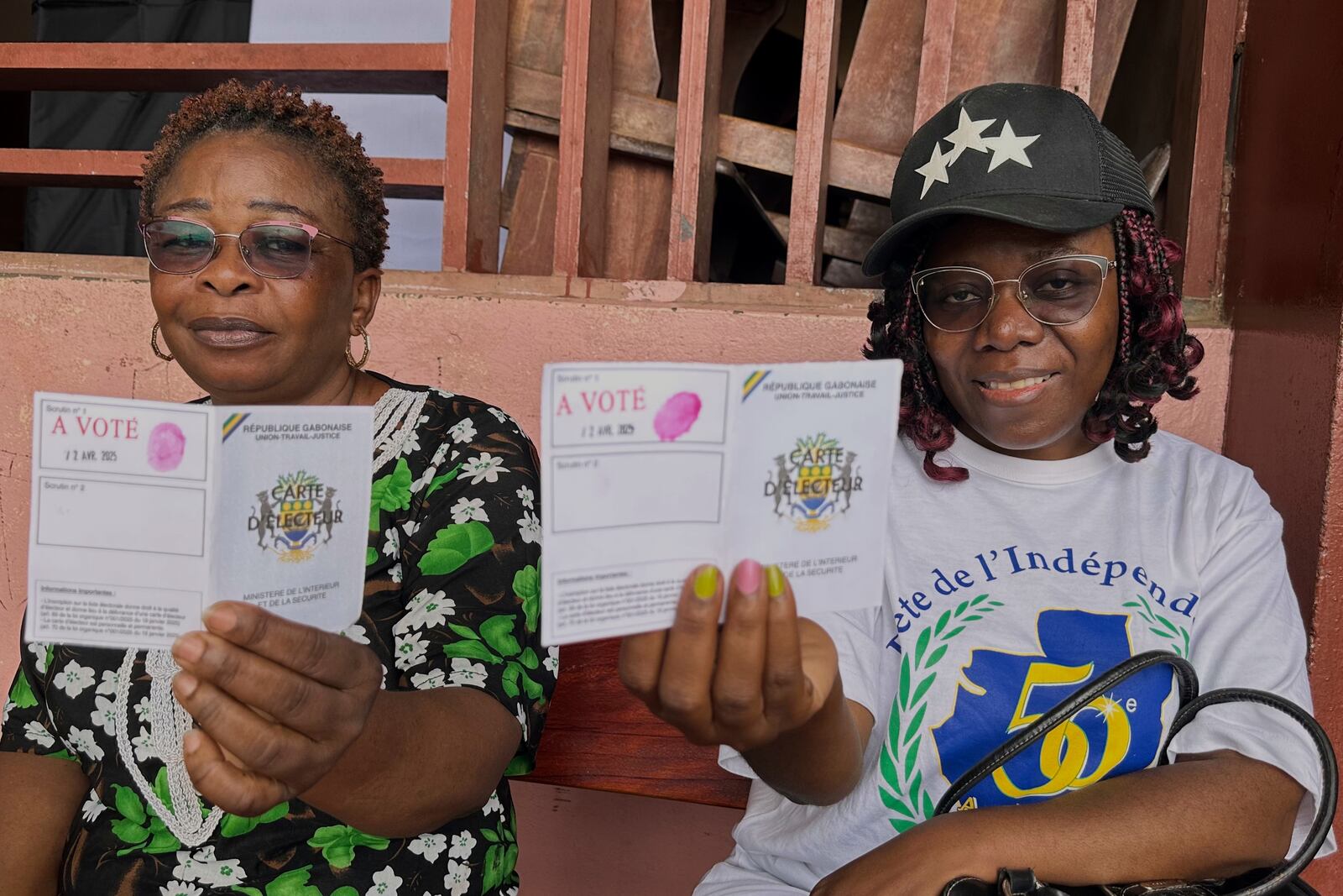 Voters display their voting cards outside a polling station during the presidential elections, in Liberville, Gabon, Saturday, April 12, 2025. (AP Photo/Betines Makosso)