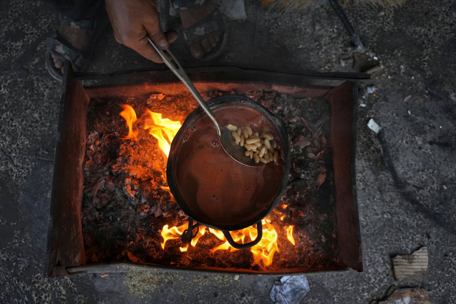 A Palestinian mother cooks beans over a fire fueled by burning plastic at a tent sheltering displaced families in Gaza City, Saturday, May 24, 2025. (AP Photo/Jehad Alshrafi)