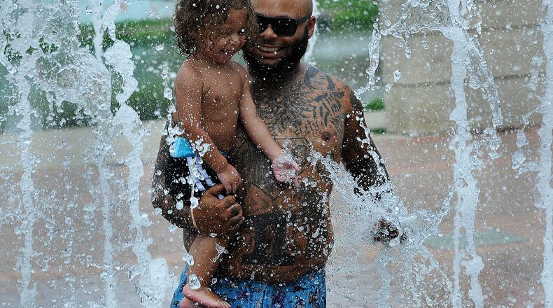 Chris Harris cools off Tuesday July 25, 2023 with his son Cali, age 2, at the splash pad at the Riverscape. MARSHALL GORBY\STAFF