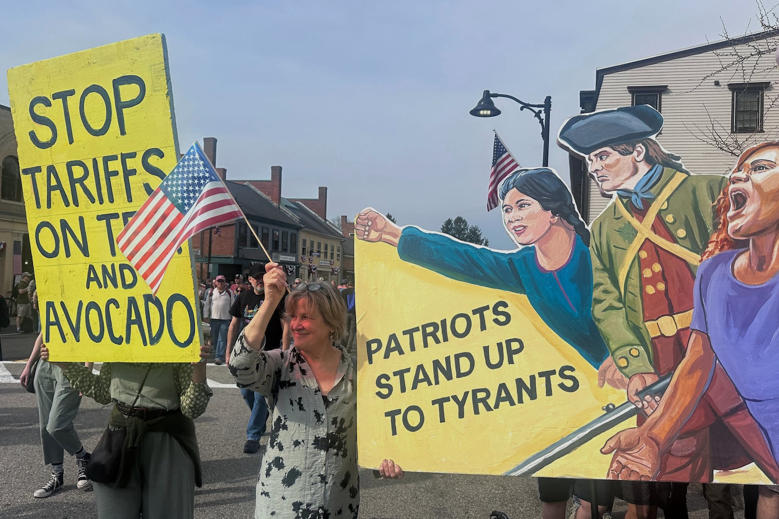 Protesters hold signs during a parade honoring the 250th anniversary of the American Revolution, Saturday, April 19, 2025, in Concord, Mass. (AP Photos/Michael Casey)