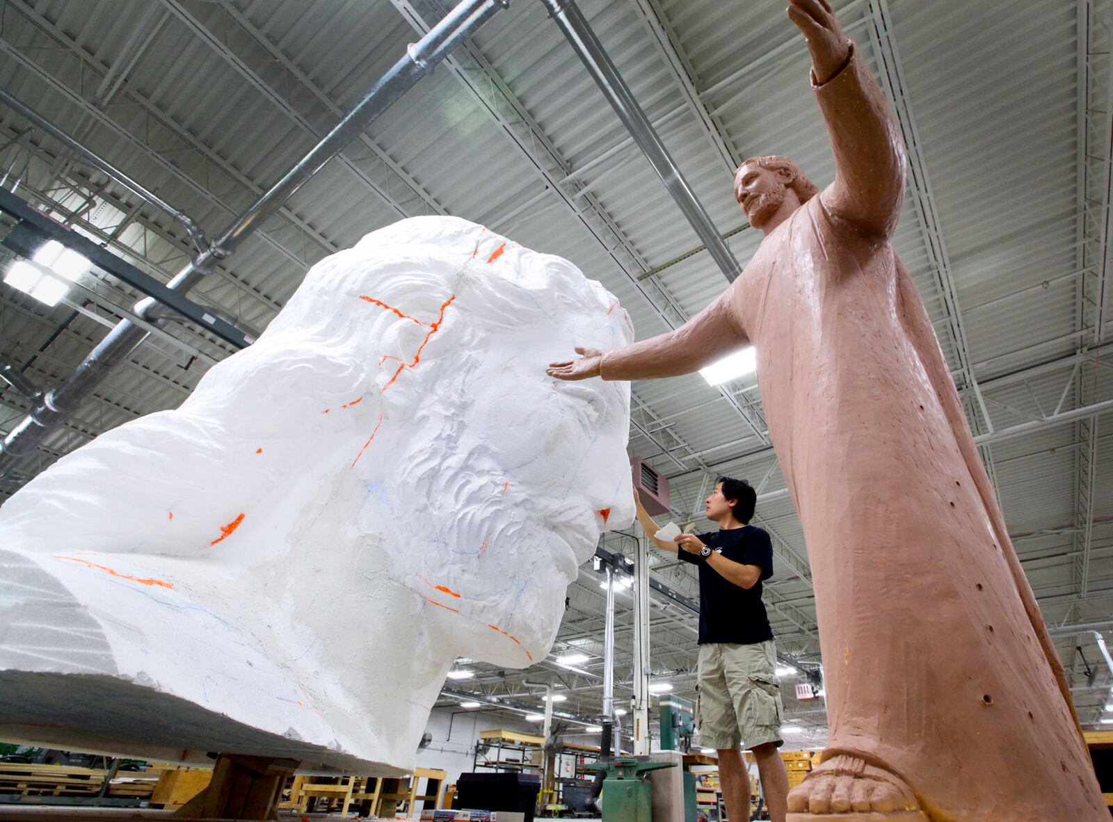 Sculptor Tom Tsuchiya shapes the styrofoam head of the Solid Rock Church Jesus sculpture at Display Dynamics in Clayton. In the foreground is the 1/10th scale model of the finished statue titled "Lux Mundi." FILE