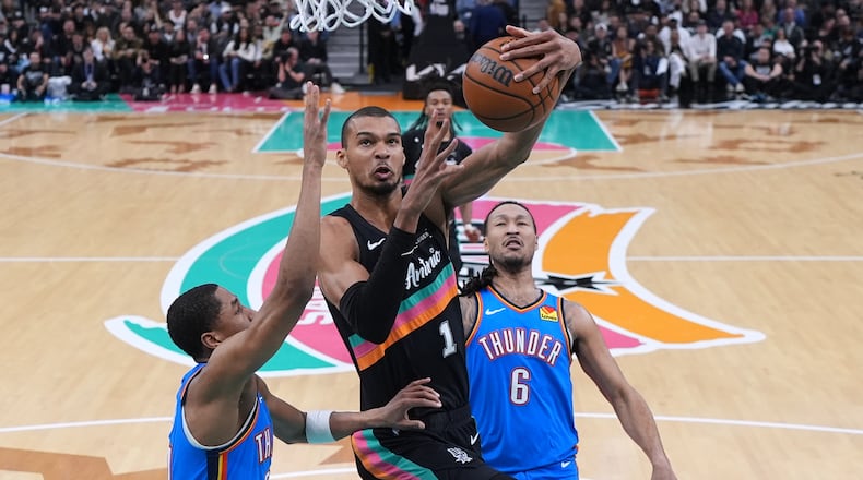 San Antonio Spurs forward Victor Wembanyama (1) drives to the basket between Oklahoma City Thunder guard Aaron Wiggins, left, and forward Jaylin Williams (6) during the second half of an NBA basketball game in San Antonio, Wednesday, February. 4, 2026. (AP Photo/Eric Gay)