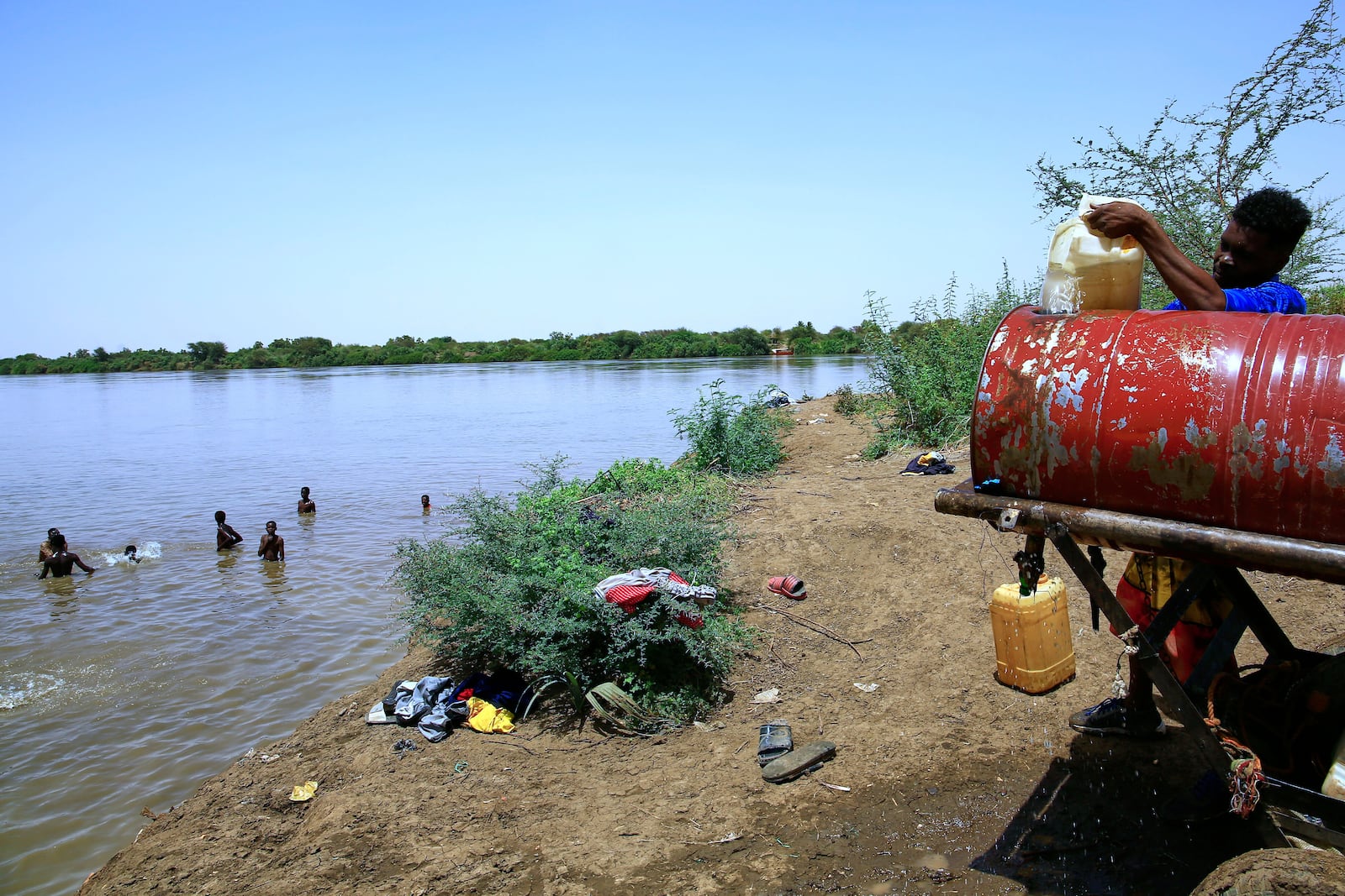 People swim in the Nile River as another fills a water container due to water outages in Khartoum, Sudan, Sunday, May 25, 2025. (AP Photo)