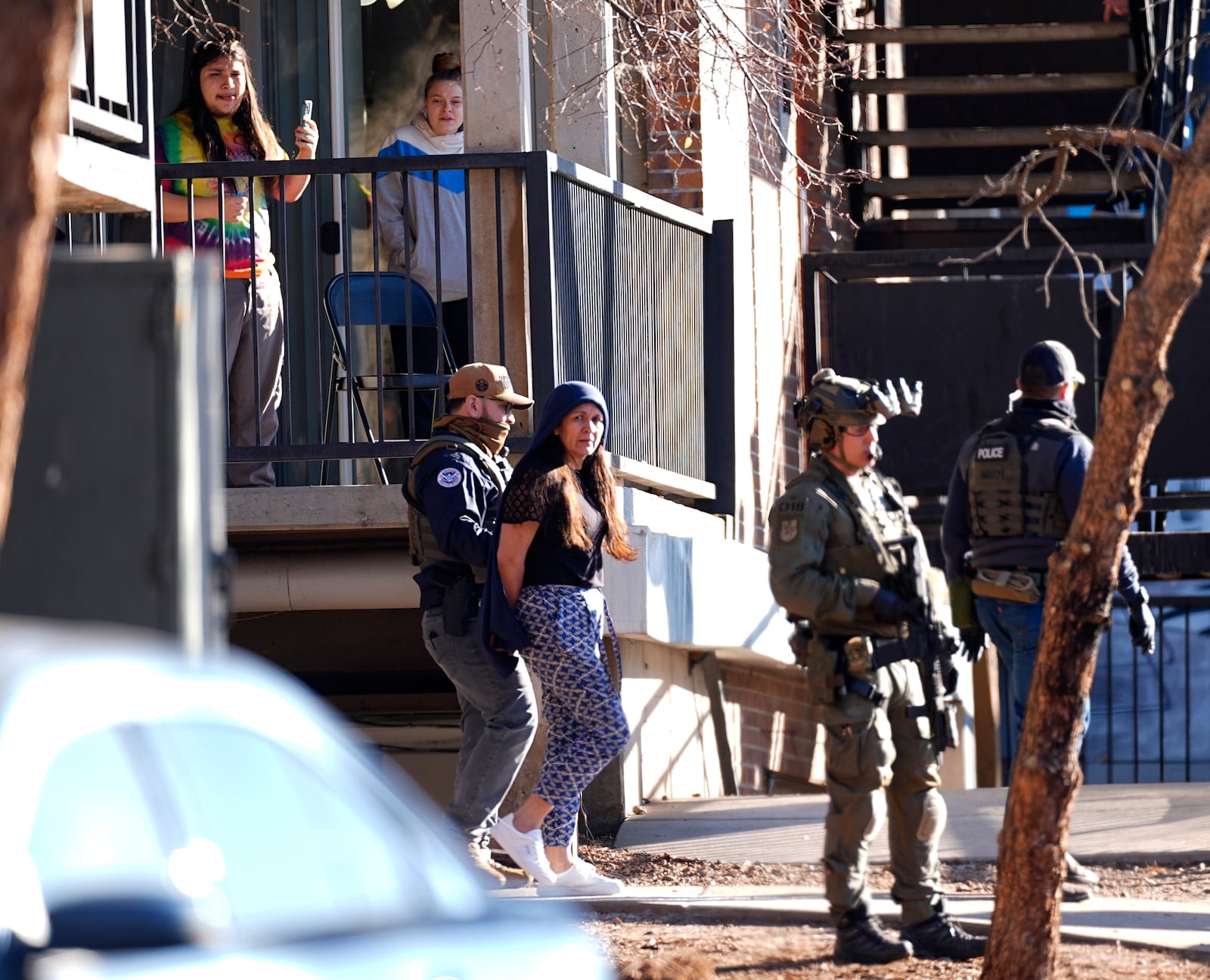 FILE - As a neighbor documents with a mobile telephone, a woman is escorted by a law officials from an apartment during a raid, Feb. 5, 2025, in east Denver. (AP Photo/David Zalubowski, File)