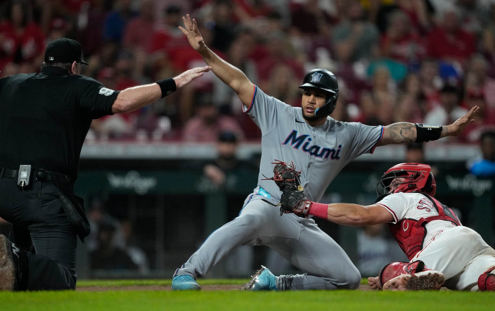 Cincinnati Reds catcher Tyler Stephenson, right, looks to umpire Chris Conroy, left, as Miami Marlins' Agustín Ramírez, center, is safe at home plate on a single by Liam Hicks during the fifth inning of a baseball game in Cincinnati, Monday, July 7, 2025. The Reds challenged but the call on the field was upheld. (AP Photo/Carolyn Kaster)