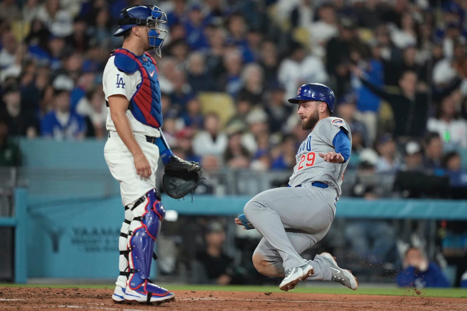 Chicago Cubs' Michael Busch, right scores on a sacrifice by Nico Hoerner as Los Angeles Dodgers catcher Austin Barnes stands at the plate during the seventh inning of a baseball game Saturday, April 12, 2025, in Los Angeles. (AP Photo/Mark J. Terrill)