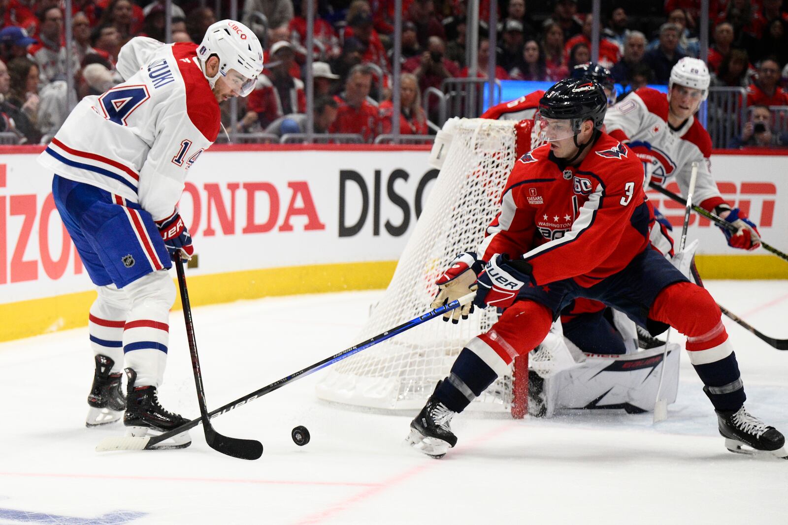 Montreal Canadiens center Nick Suzuki (14) and Washington Capitals defenseman Matt Roy (3) battle for the puck in the second period of Game 1 of a first-round NHL hockey playoff series Monday, April 21, 2025, in Washington. (AP Photo/Nick Wass)
