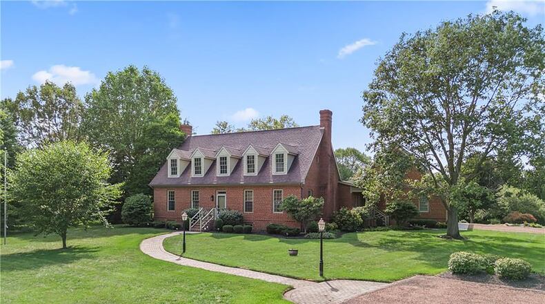 The front of the Cape Cod style brick story and a half has dormers, brick paver walkway and brick steps leading to the front door.
