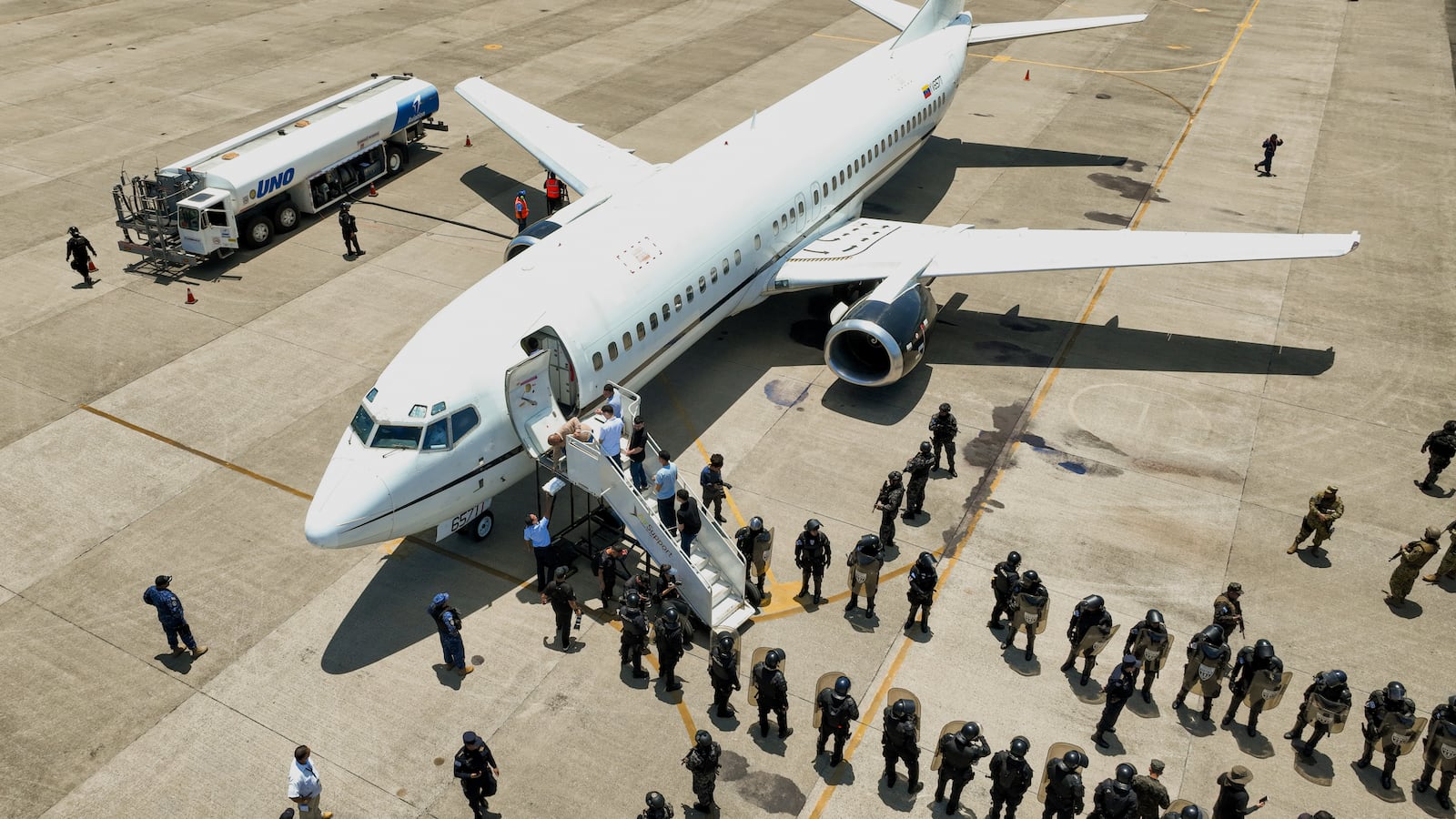 This photo released by the El Salvador's presidential press office shows men, who El Salvador's government identify as Venezuelans who the U.S. government detained and flew to El Salvador months ago, boarding a Venezuelan plane bound for Venezuela as soldiers stand by at the Oscar Arnulfo Romero International Airport in San Luis Talpa, El Salvador, Friday, July 18, 2025. (El Salvador's presidential press office via AP)