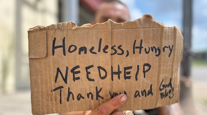 A panhandler holds a sign asking for help near downtown Dayton on July 20, 2023. Dayton is going to launch a new crisis response unit that will help people who struggle with mental and behavioral health issues, likely including homeless individuals. CORNELIUS FROLIK / STAFF