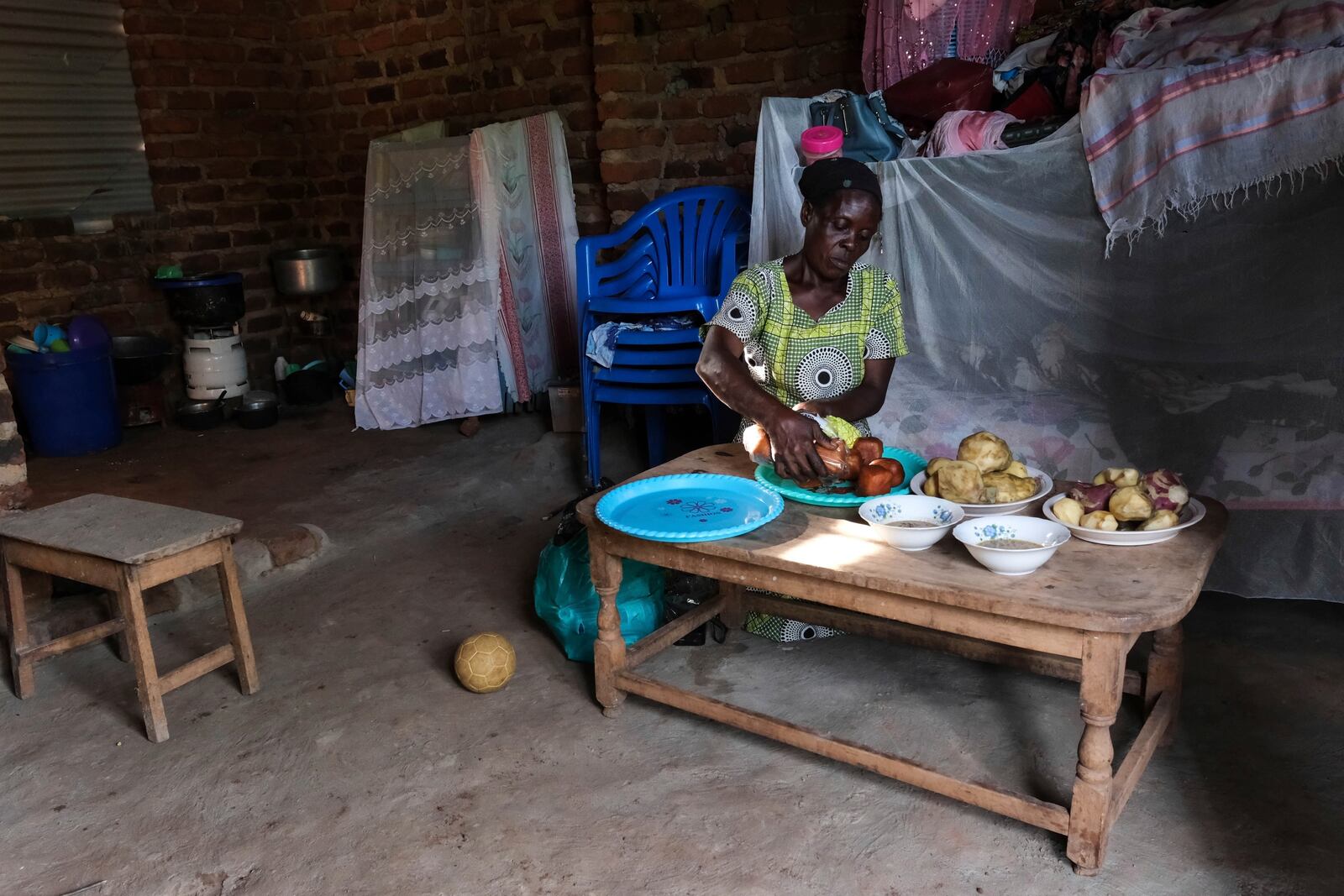 Rehema Namukose prepares a meal inside her home with clay-based earthen floors installed by EarthEnable on May 17, 2025, in Jinja, Uganda. (AP Photo/Hajarah Nalwadda)