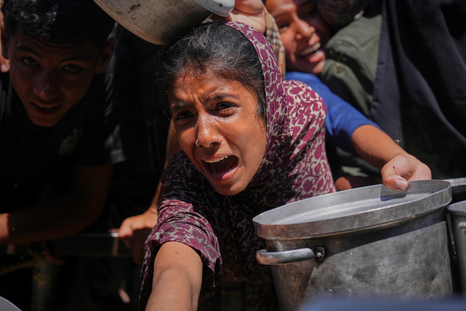 Palestinians struggle to receive cooked food distributed at a community kitchen in the Muwasi area of Khan Younis, in the Gaza Strip, Friday, May 23, 2025. (AP Photo/Abdel Kareem Hana)