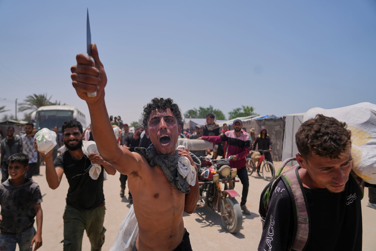 A Palestinian shouts to the camera in Arabic "We get food with the taste of death and blood" as he carries a bag containing food and humanitarian aid packages delivered by the Gaza Humanitarian Foundation, a U.S.-backed organization, in Rafah, southern Gaza Strip, Tuesday, June 10, 2025. (AP Photo/Abdel Kareem Hana)